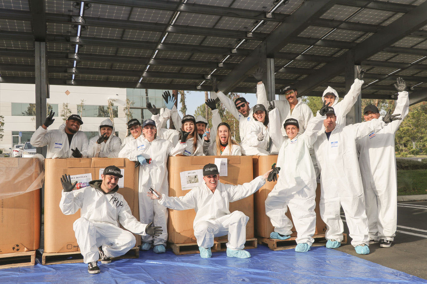 Dr. Bronner's employees in white coveralls and All-One hats, arms raised