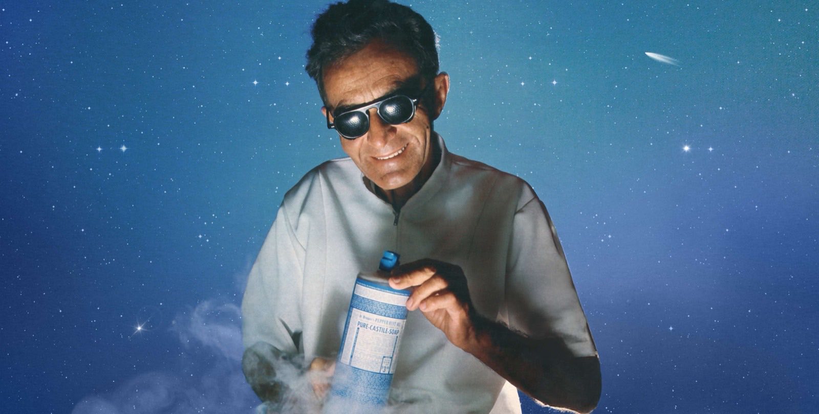 Emanuel Bronner holding a bottle of Pure-Castile Soap against a starry sky
