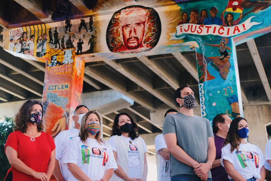 A community gathering in front of a Justicia mural