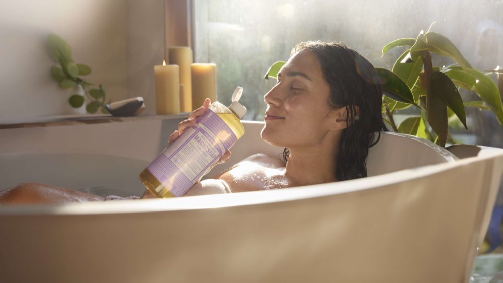 A woman relaxing in a bath with a bottle of lavender Magic Soap
